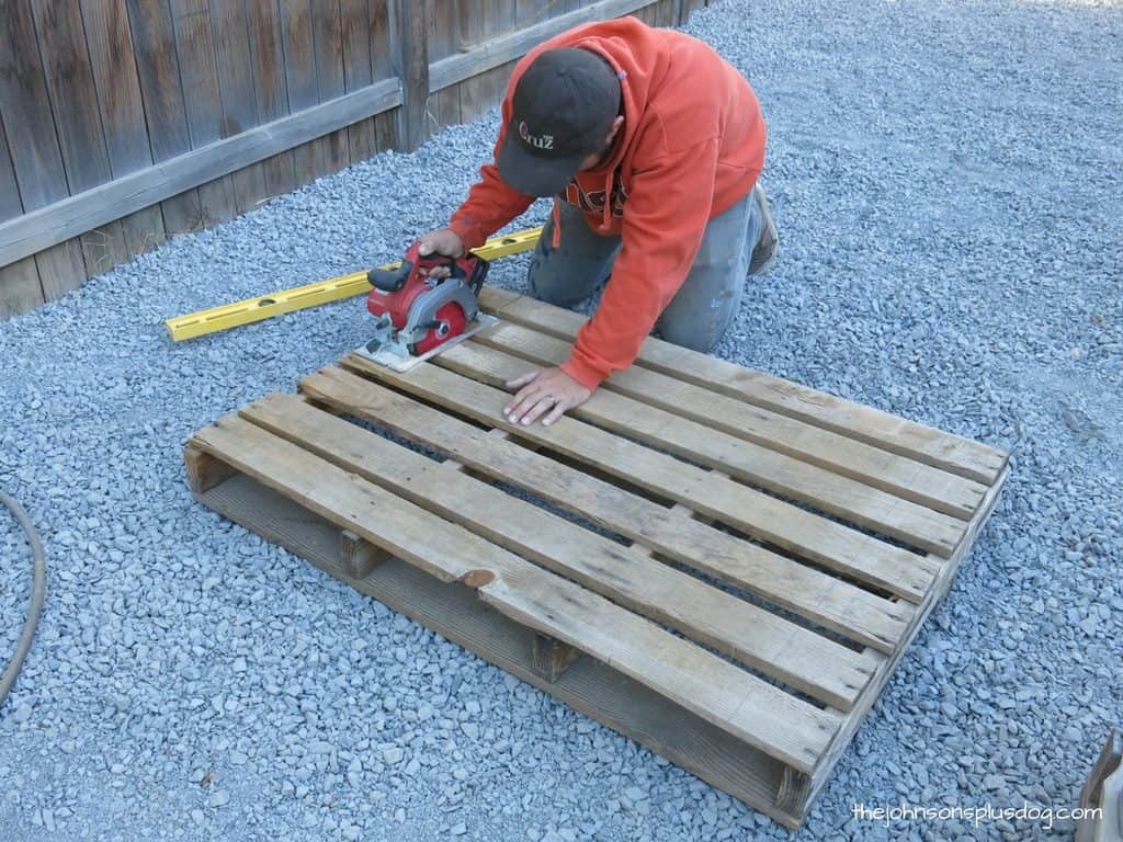 A man cuts the wood pallets down to size using a hand-held circular saw. This pallet will soon be transformed into a DIY pallet wood AC unit cover.