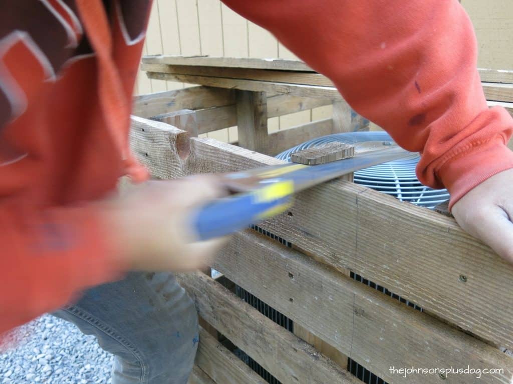 Using a hand saw to trim off the excess wood from one of the wood AC unit cover support pillars.