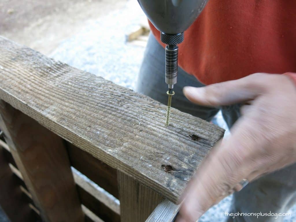 Using a power drill to drill screws into bars of pallet wood. These tops bars really round out the wood AC unit cover, making it look more complete!