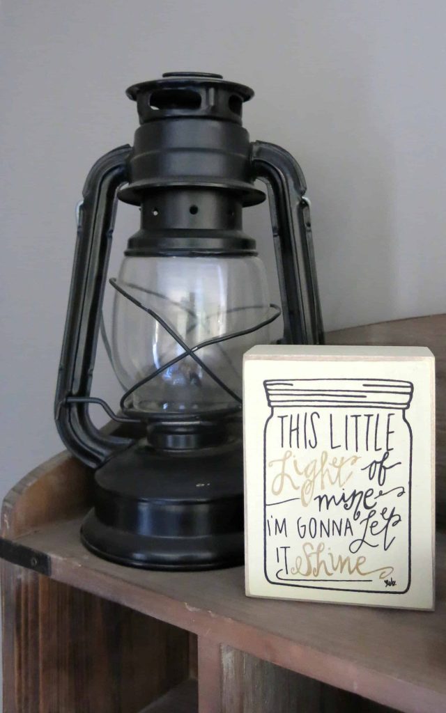 black metal camping lantern and a small sign that reads "this little light of mine, I'm gonna let it shine"