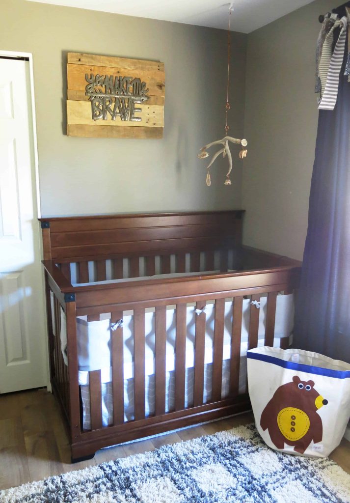 a wooden crib with a metal sign above it that says "you make me brave," and an antler mobile hanging above the crib