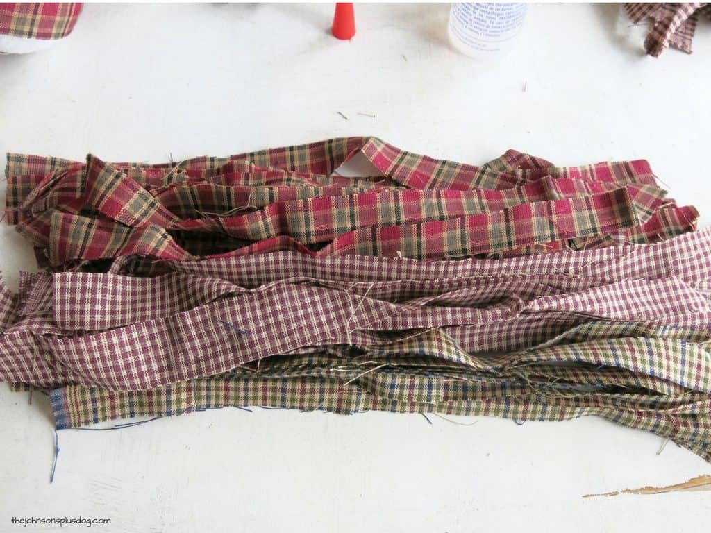 Strips of homespun fabric, laid out on a white table, ready to turn into homemade fabric ornaments