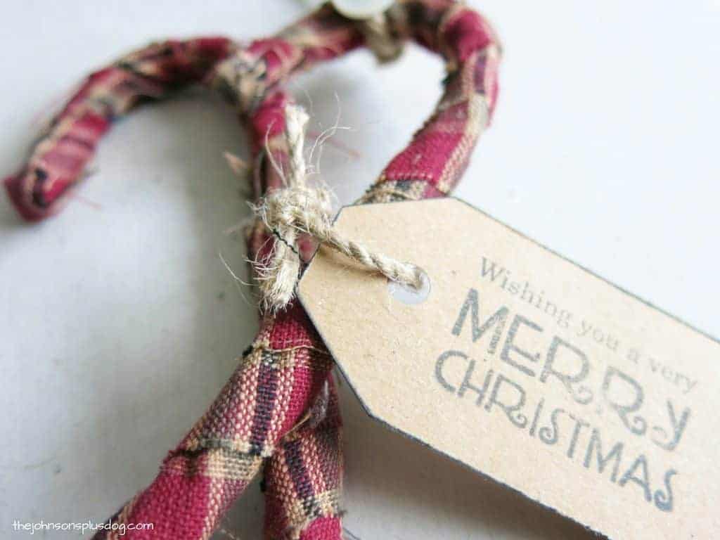 A stamped gift tag attached to the fabric wrapped candy cane ornaments with jute twine.