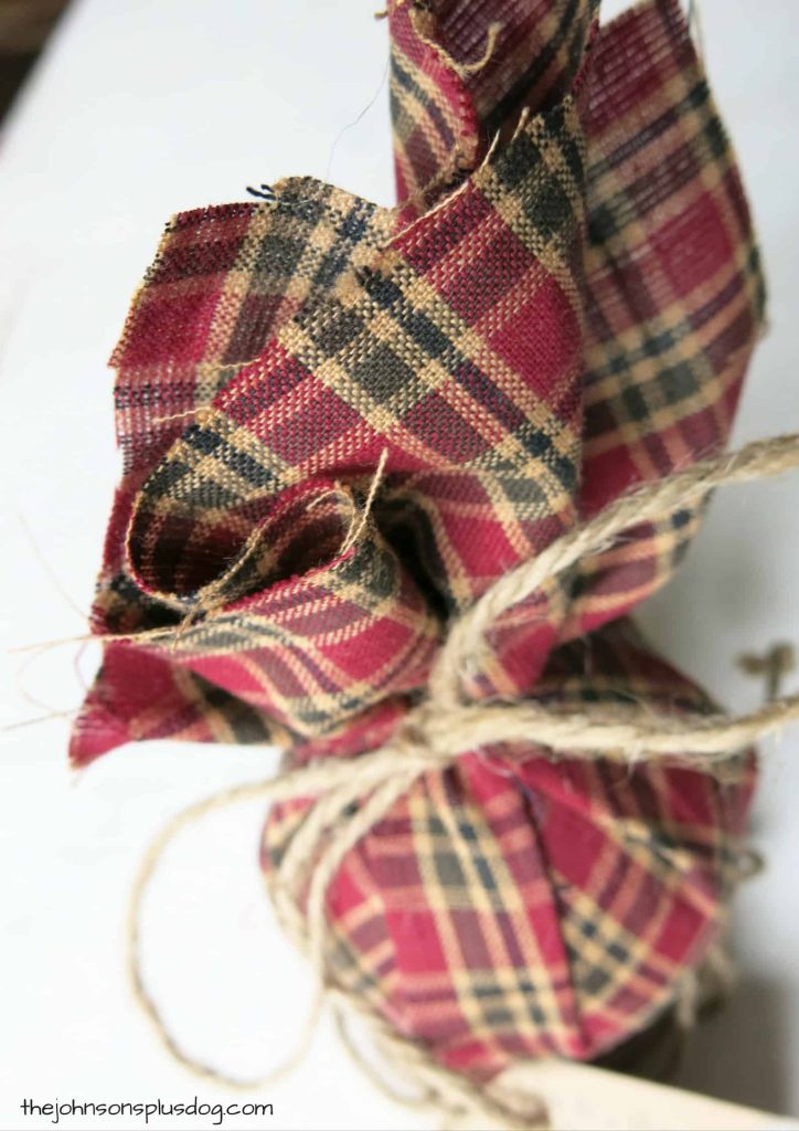 A slightly out-of-focus overhead shot of a homemade fabric ornament - red and green plaid fabric tied with jute string.