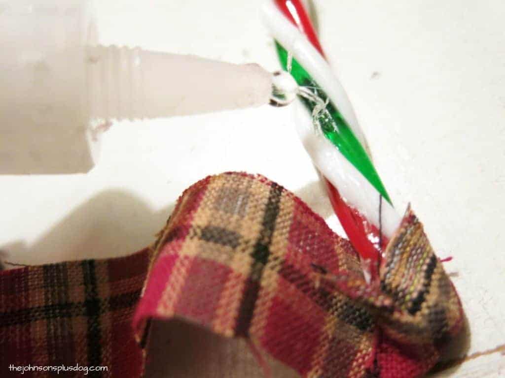 Applying craft glue to the plastic candy canes to adhere strips of plaid homespun fabric to create candy cane fabric ornaments.