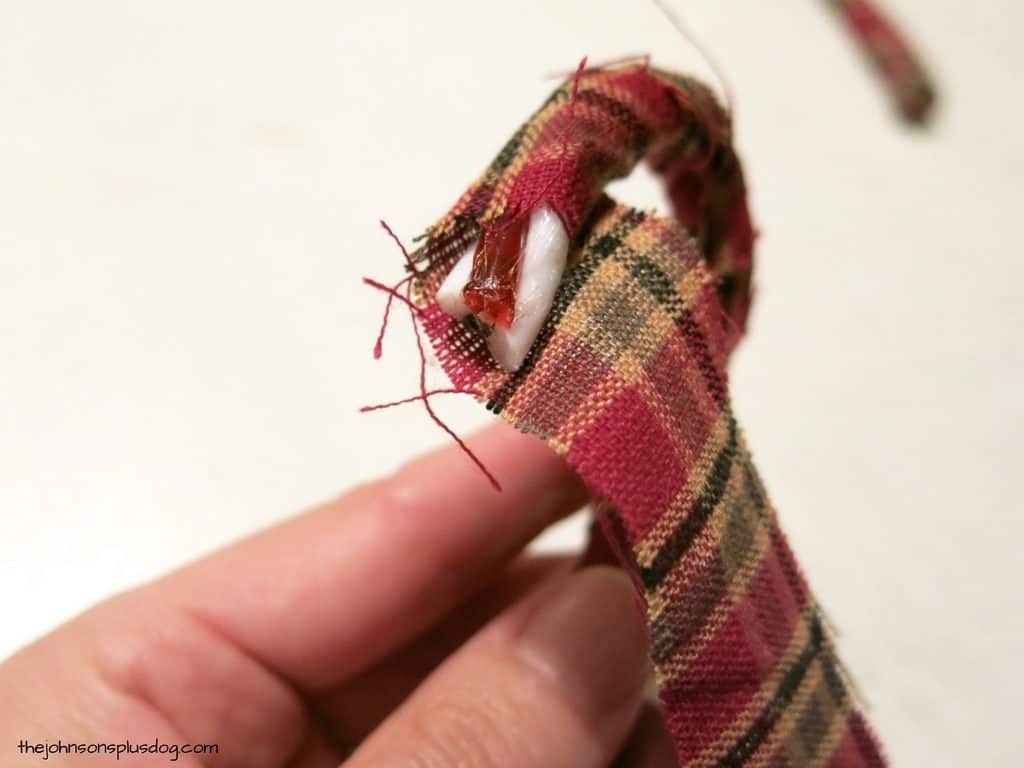 Wrapping a strip of homespun fabric around the curved cane of a plastic candy cane to create homemade fabric ornaments.