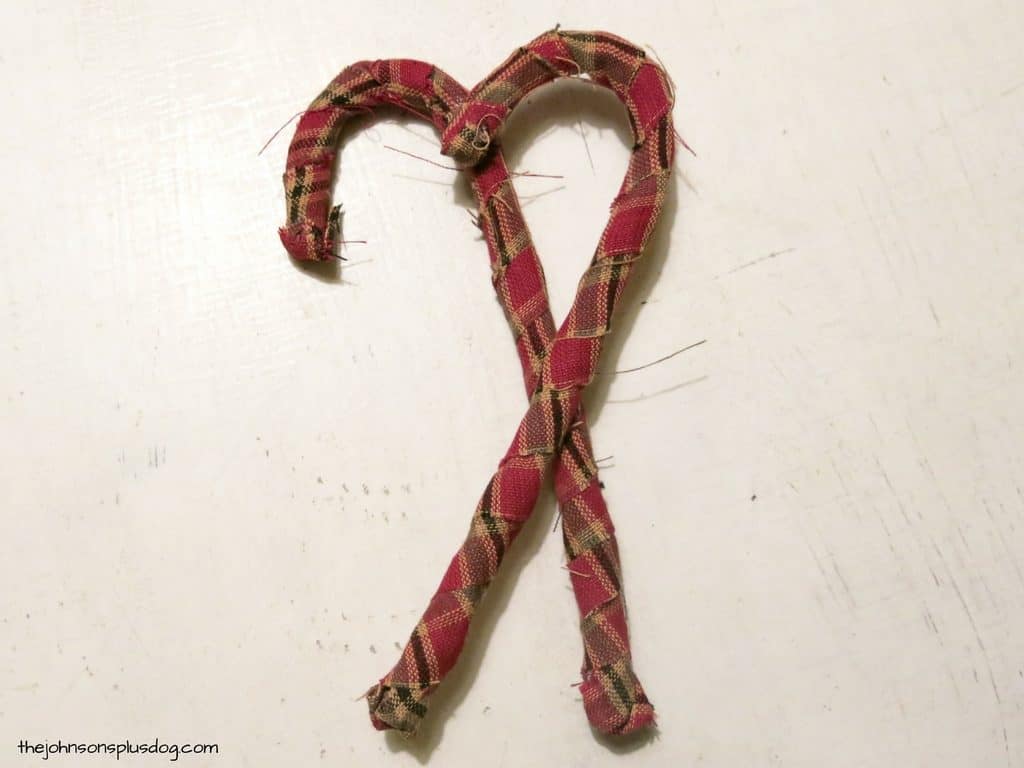 Two fabric-wrapped candy canes sit crisscrossed over each other, held together with craft glue.
