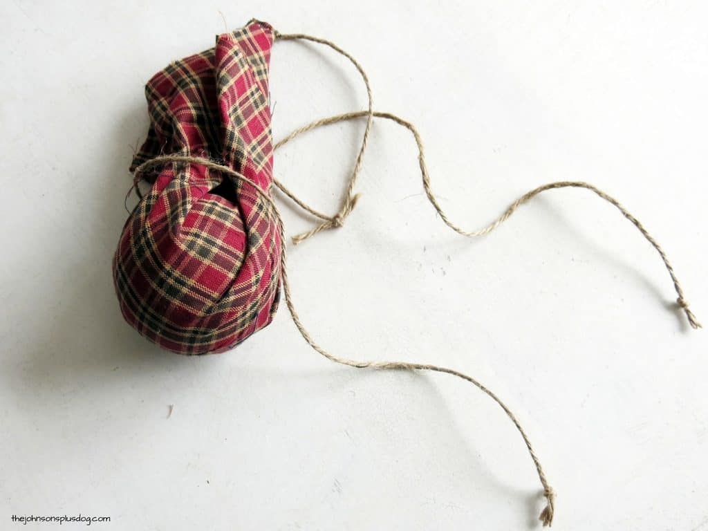 A foam ball covered in red and green plaid homespun fabric, tied with jute twine.