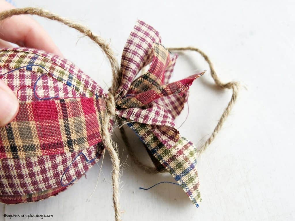 A homemade fabric ornament, the top of the homespun fabric strips tied together with a jute string.