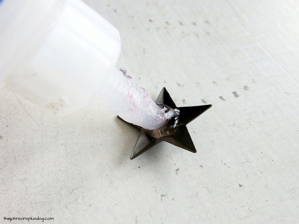 Applying craft glue to the back of a rustic metal star, which will decorate the homemade fabric ornaments.