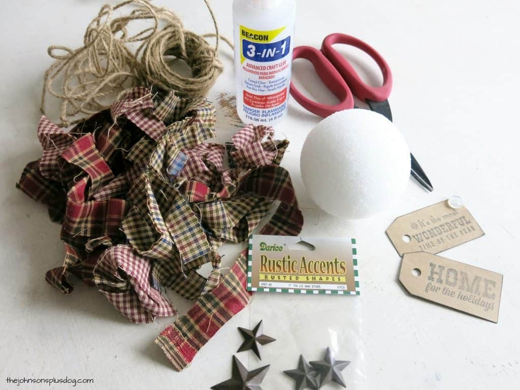 Supplies needed to make a homemade fabric ornament - you'll need fabric strips, jute string, craft glue, scissors, a foam ball, and various rustic decor accents.
