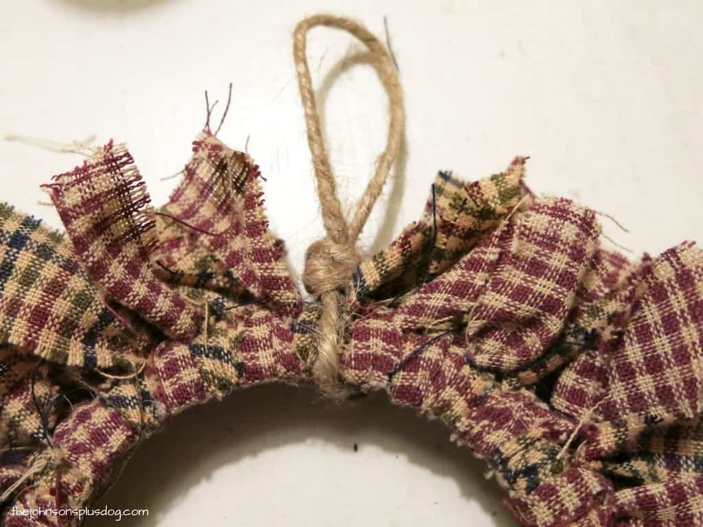 A loop of jute twine neatly tied with a knot around a mini fabric wreath fabric ornament.