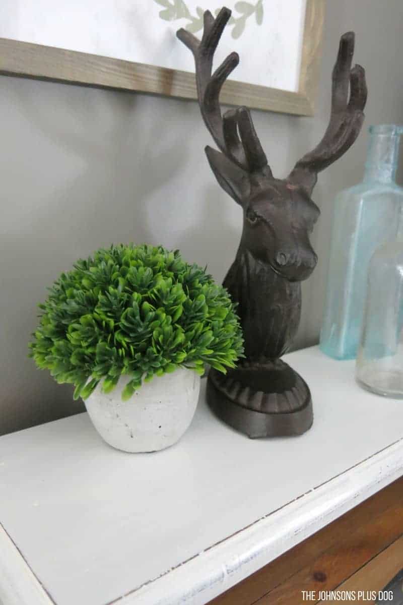 We decorated the top of our vintage bread box with some farmhouse style trinkets like a mini faux boxwood plant, a metal deer head, and vintage bottles