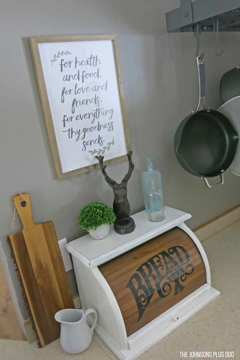 The vintage bread box sits on the countertop under a farmhouse style wood sign from Hobby Lobby that reads 