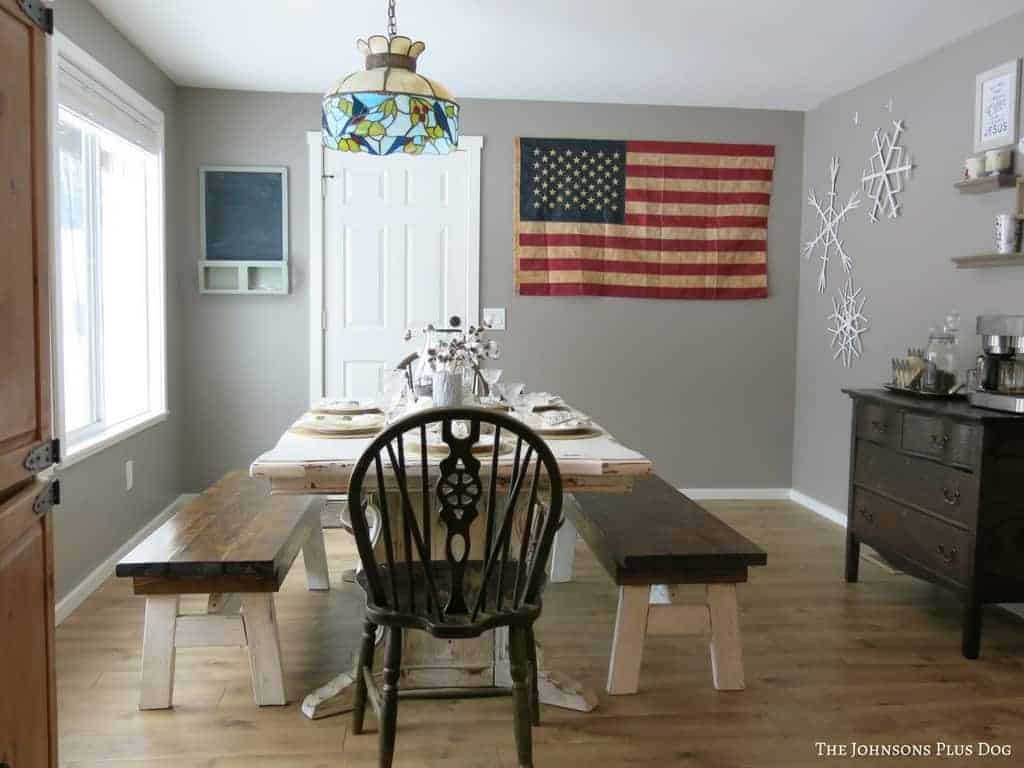 Another view of the updated dining room featuring farmhouse decor, a large dining table and benches, hardwood floors and gray painted walls.