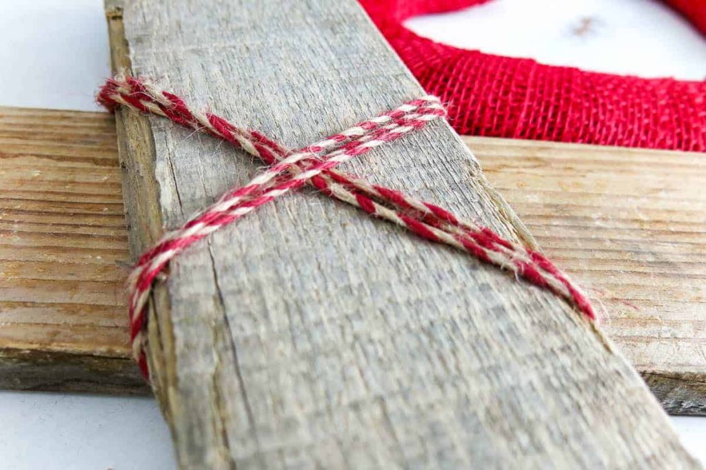 Tie two pieces of reclaimed pallet wood together with red and tan baker's twine on a Xoxo Decor.