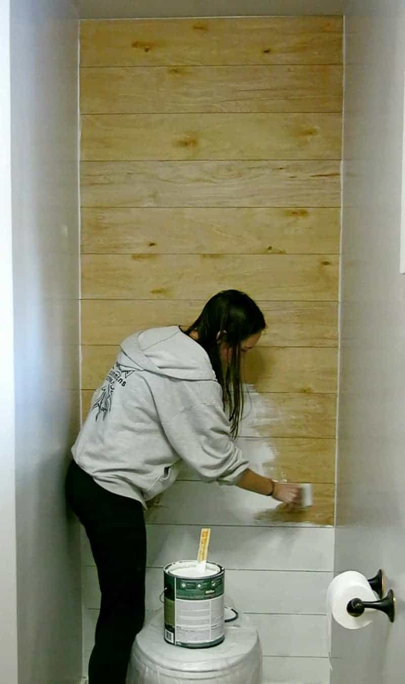 Using a paint brush to paint the wood faux shiplap wall in our bathroom nook.