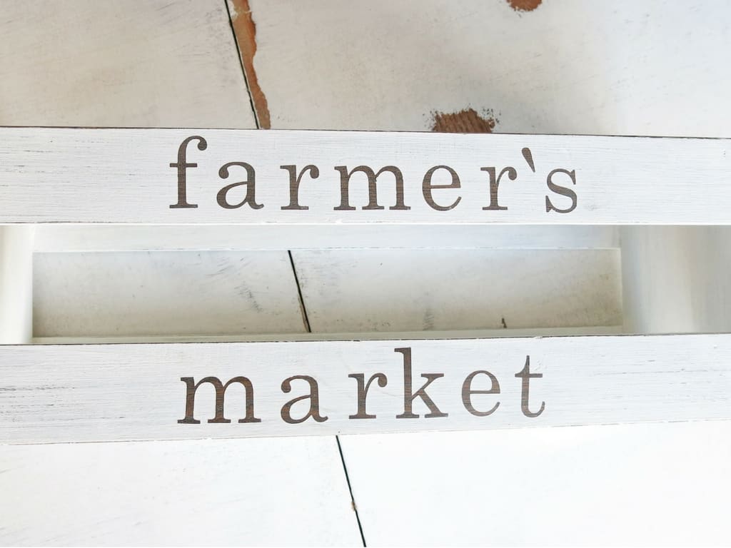 A close up look at the words "farmer's market" on the side of a white painted wooden crate. 