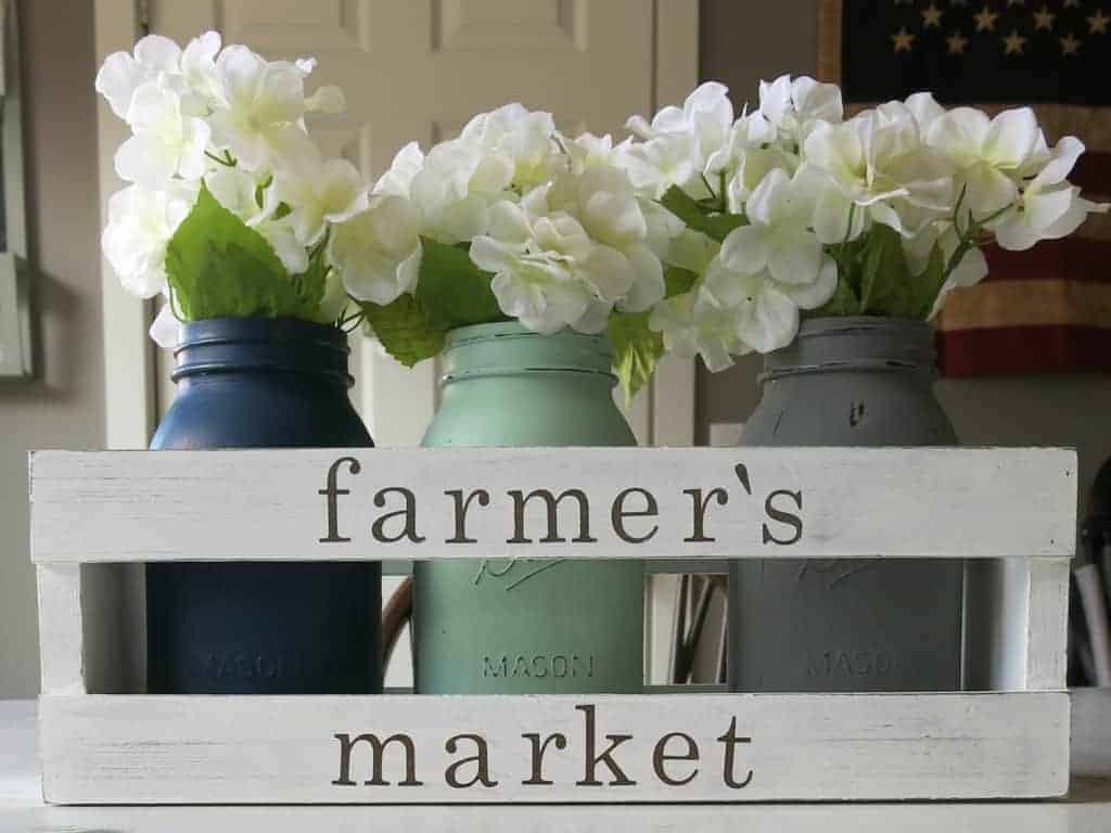 A side-angled view of a farmhouse style crate centerpiece. The white-painted wooden crate has the words 