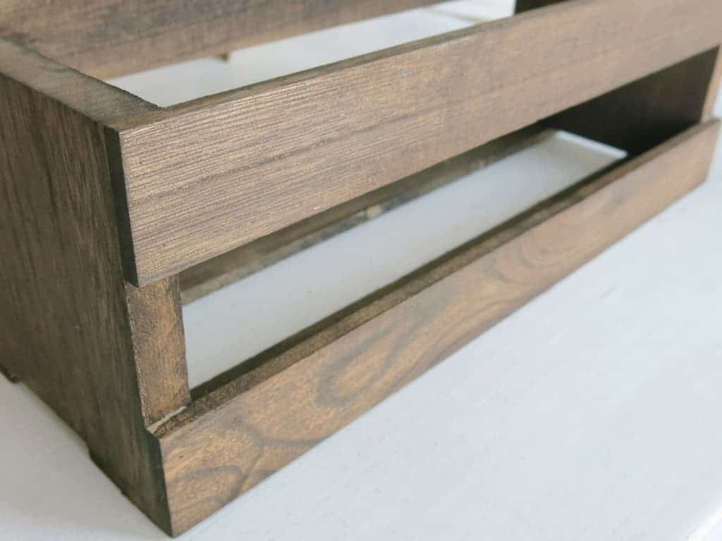 A closeup side-angled view of a wooden crate that's been stained a dark chestnut brown color. This wooden crate will be used for a farmhouse style centerpiece.