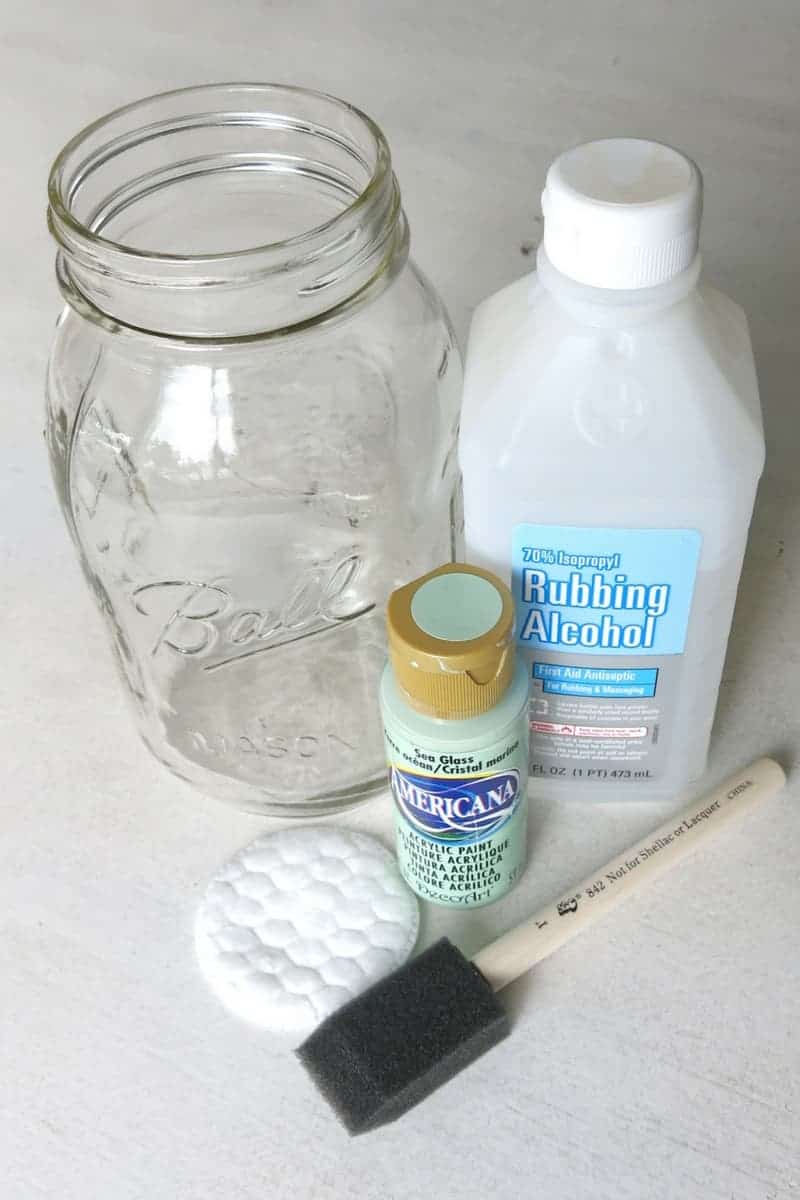 Clear glass mason jar sitting next to bottle of rubbing alcohol, craft paint, foam paint brush and cotton pad