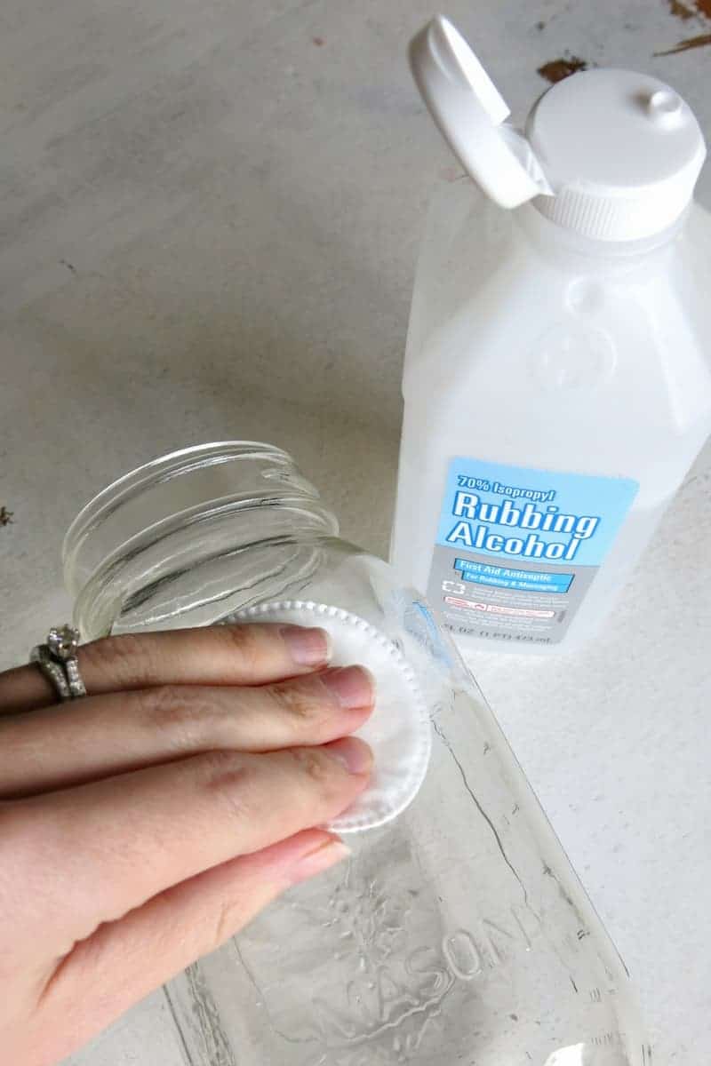 Women's hand holding a cotton pad on clear glass mason jar with rubbing alcohol to clean it