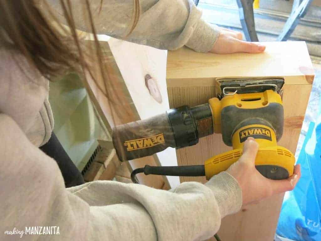 Woman sanding wooden shelf with DeWalt hand sander