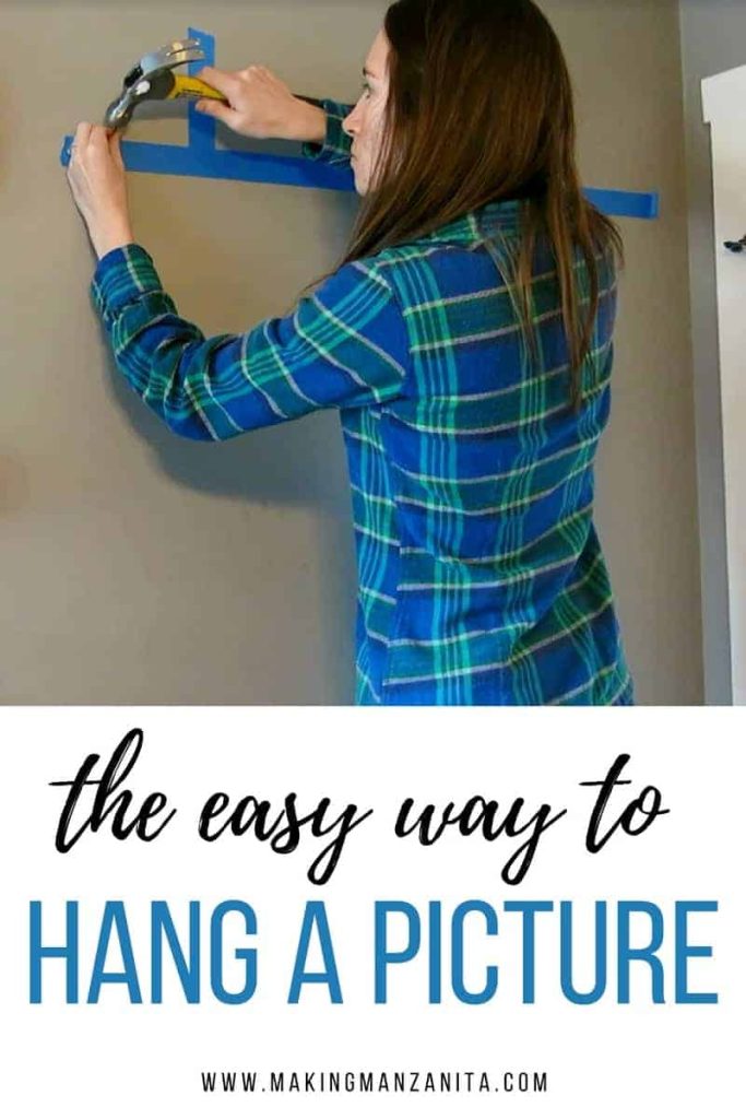 The Easy Way To Hang A Picture | a woman in a green and blue plaid shirt holds a hammer, and hammers a nail into a wall on a line of blue painter's tape.