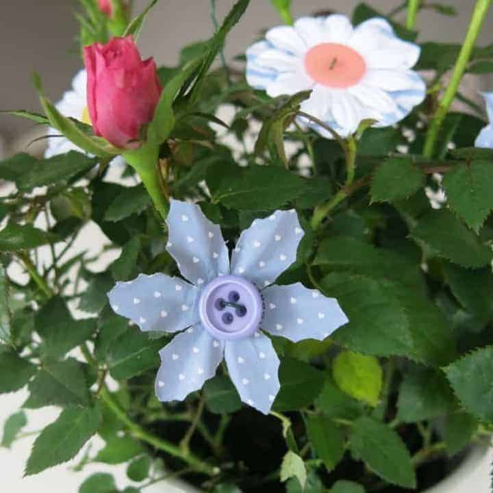 Button flowers made with floral wire, paper flowers and buttons sticking out of potted mini rose plant sitting on white table