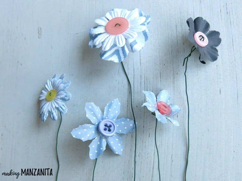 5 completed button flowers sit on a white table. We'll use these adorable little faux flowers to create the "moms are like buttons" craft for Mother's day.