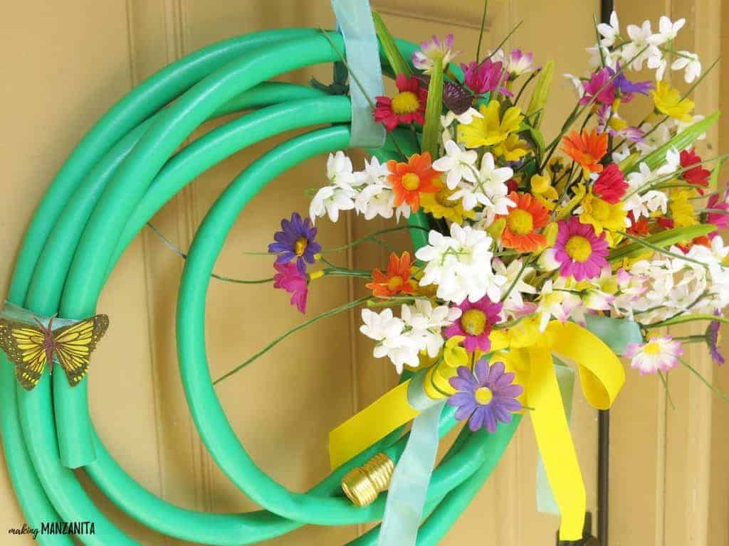 A colorful spring wreath made with an upcycled garden house and bouquet of Spring colored faux flowers tied with ribbon.