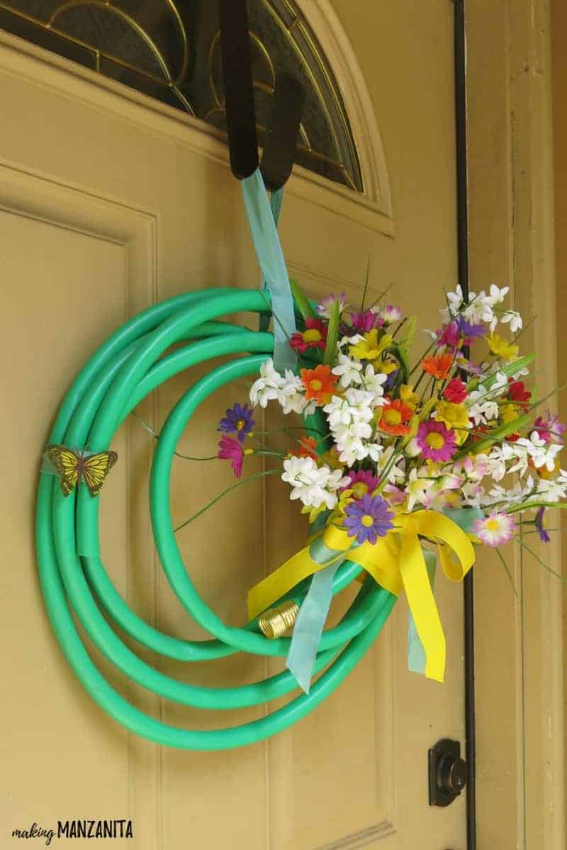 An upcycled garden hose wreath with faux floral bouquet hangs on a front door wreath hanger.