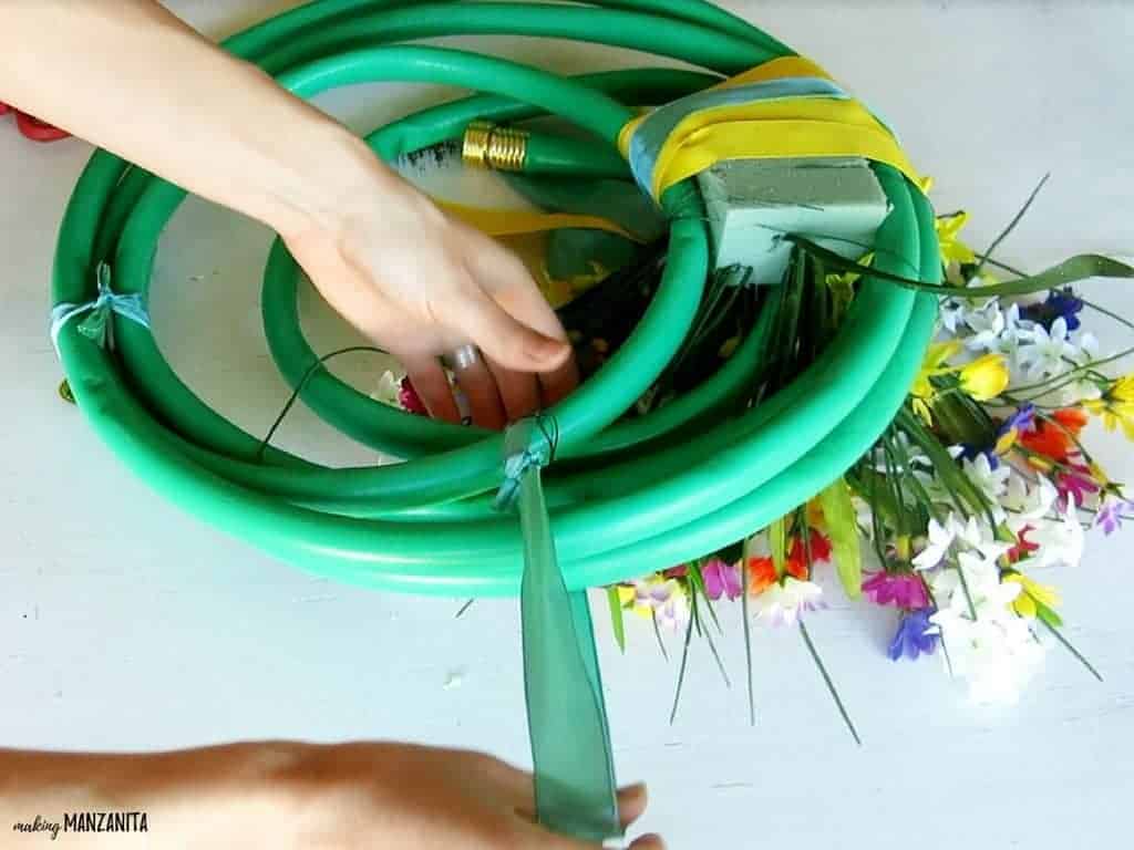 Attaching a ribbon hanger to the garden hose wreath using blue ribbon.