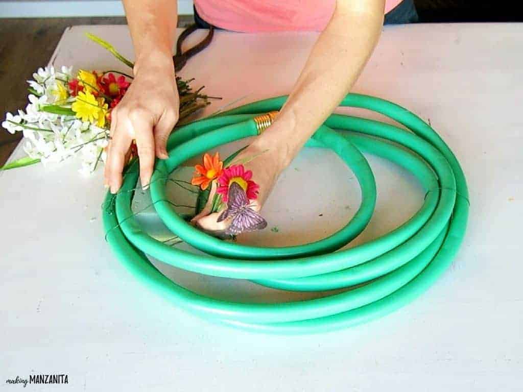 A woman attaches the faux flowers to the floral foam block, wrapped up in the garden hose to create a colorful Spring upcycled garden hose wreath.