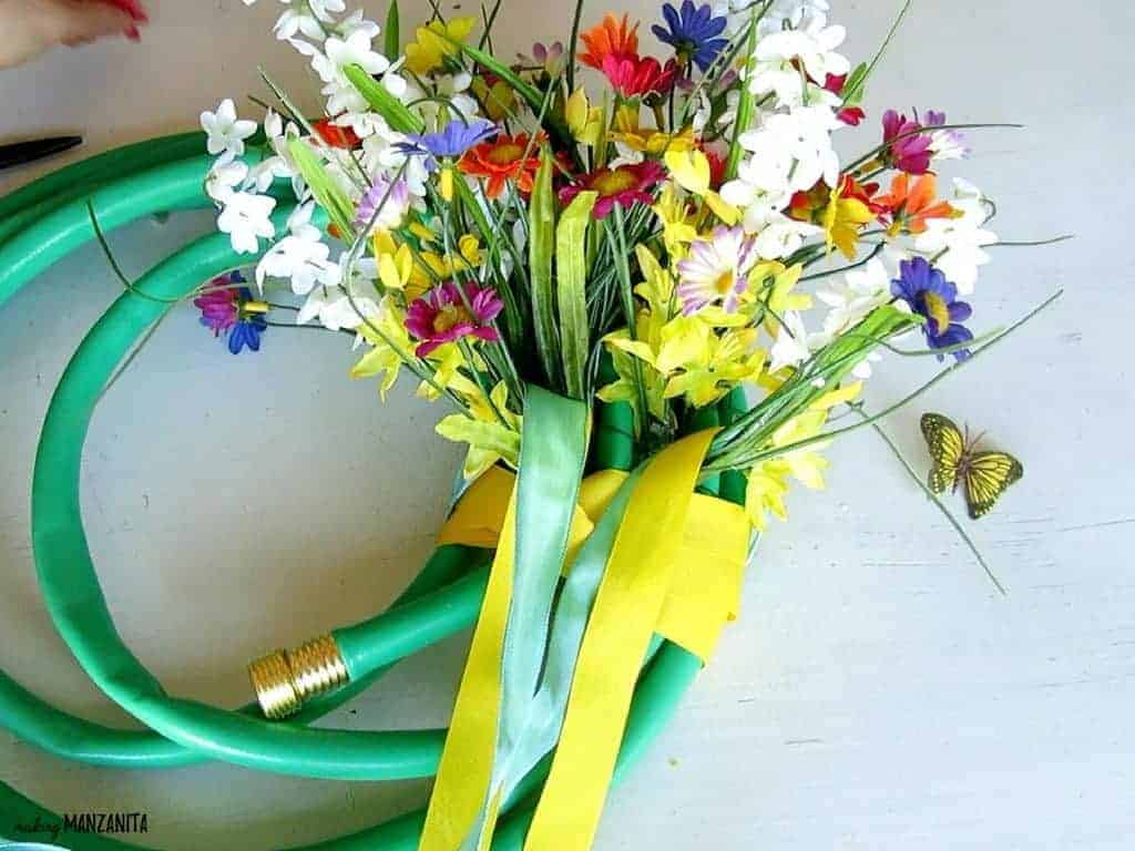 Wrapping wide yellow and blue ribbon around a bouquet a flowers on an upcycled garden hose wreath.