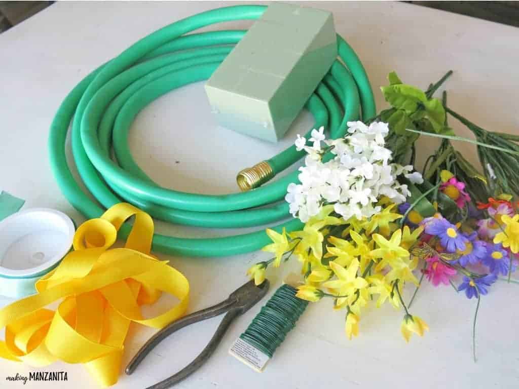 Supplies needed to make a Spring garden hose wreath laid out on a table: an upcycled garden hose, floral foam block, faux flowers, ribbon, floral wire, and wire cutters