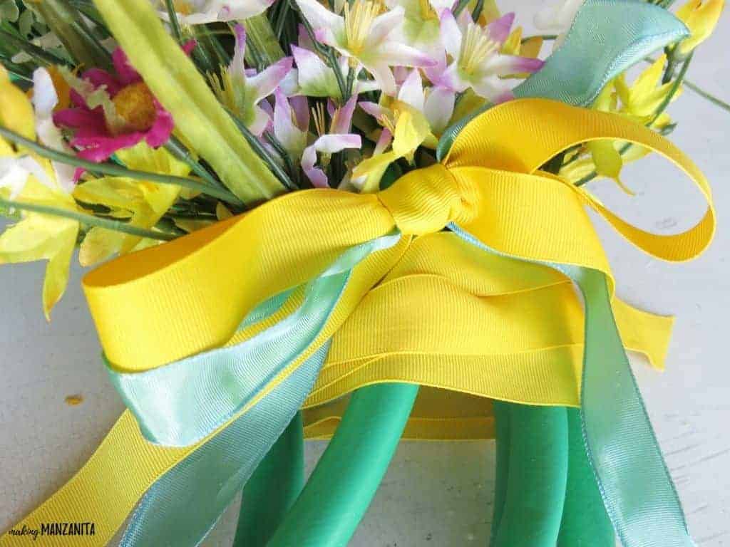 A close up shot of the yellow and blue ribbon tied around the garden hose wreath and faux flower bouquet.