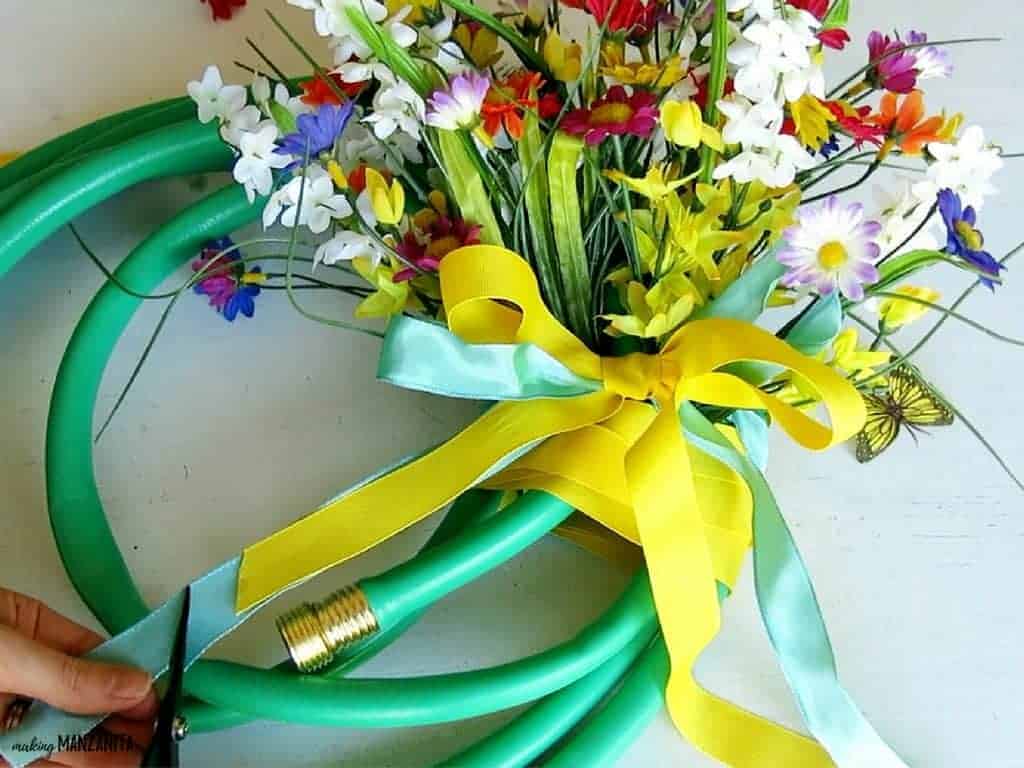 A bouquet of flowers wrapped in blue and yellow ribbon, tied in a bow. A woman uses a scissors to cut the ribbon.