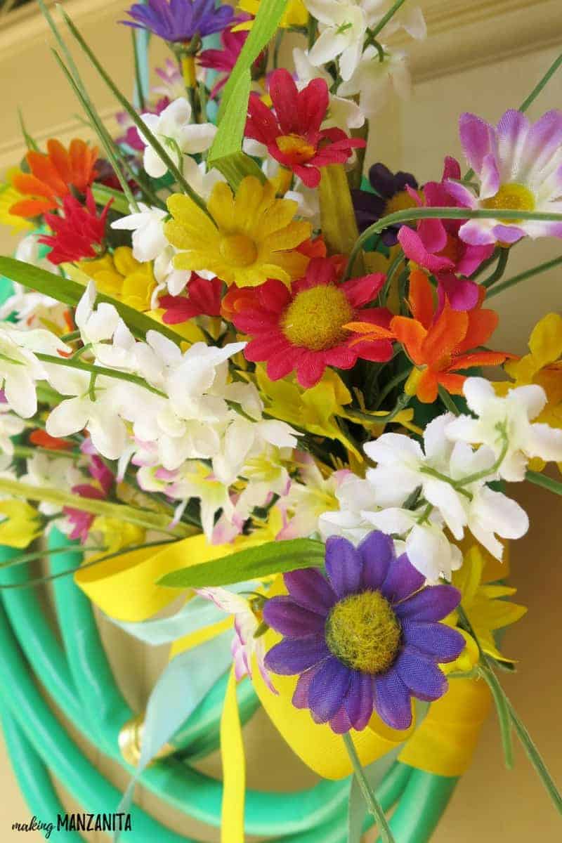 A close up look at the fake flowers used on this upcycled garden hose wreath. The bright yellow, orange, red, white, pink, and purple flowers are faux flowers from the dollar store.