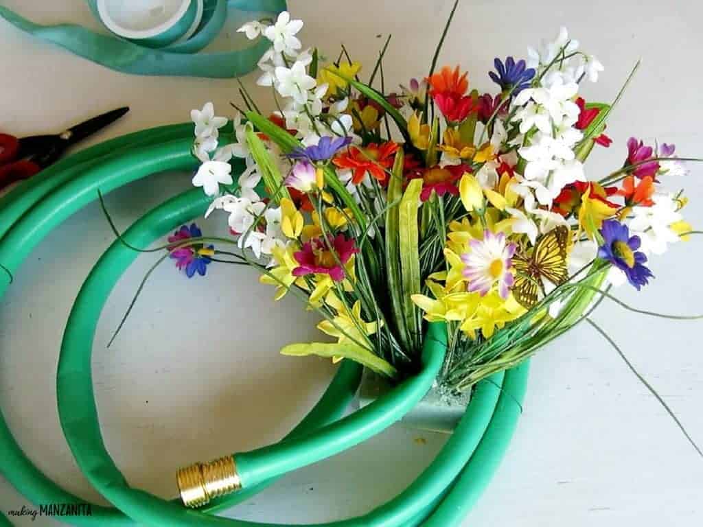 Bunches of faux flowers fill the foam block attached to the upcycled garden hose wreath.