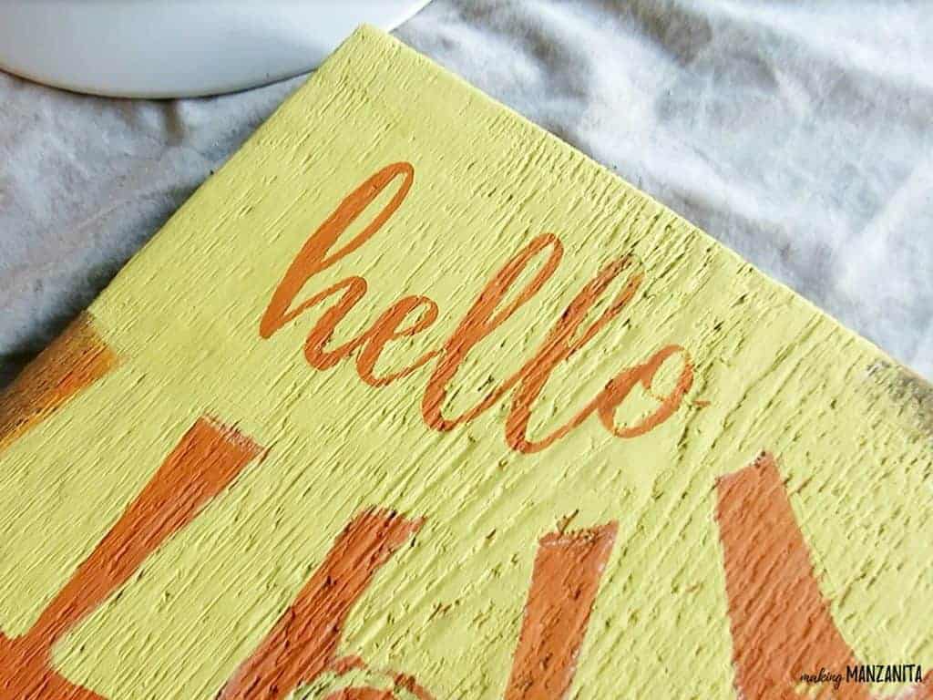 A close up shot of the word "hello" painted in orange paint, inside a sunshine shape with sun rays.