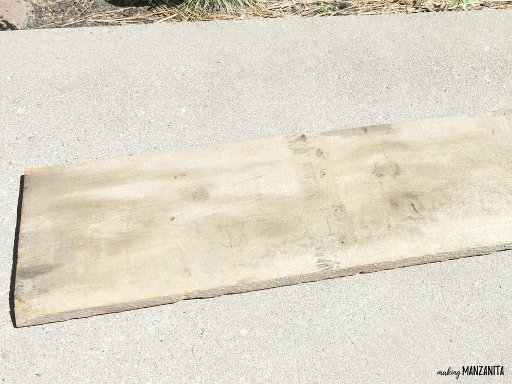 A single piece of reclaimed wood sitting on the concrete sidewalk. Follow along as we turn this weathered piece of wood into a DIY sunshine sign.