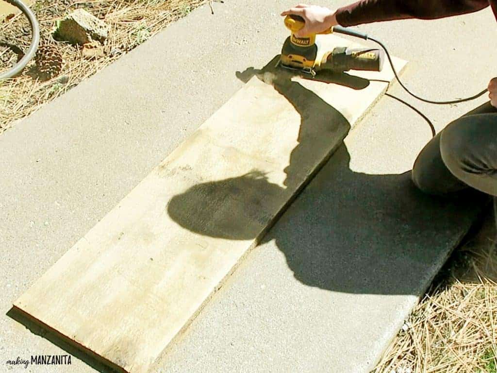 Using an electric sander to sand down the surface of the reclaimed wood board for the Hello Sunshine sign