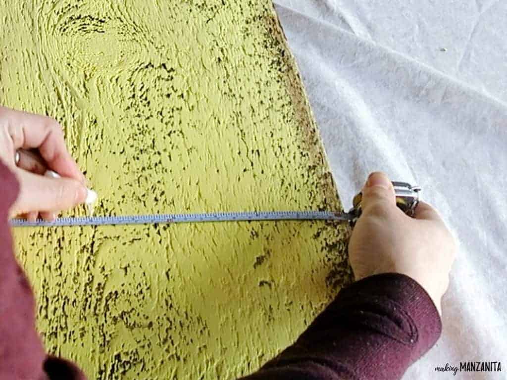 Using a thin measuring tape to measure the center point of the yellow-painted wood sign.