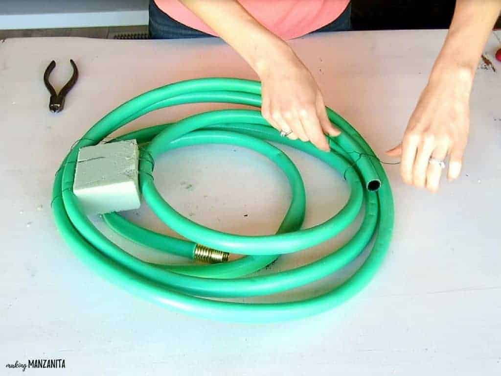 A woman wraps floral wire around the end of the garden hose, securing the hose in a wrapped wreath form.