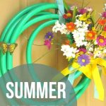 Wreath made with a garden house with fake flowers hanging on a tan door with text overlay that says summer wreath