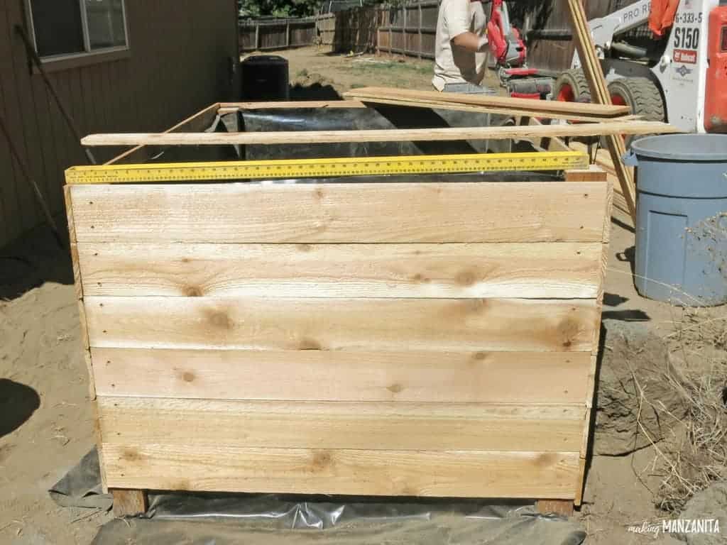 Almost done large rectangular waist tall  cedar boards attached formed into a raised garden bed with plastic lining underneath