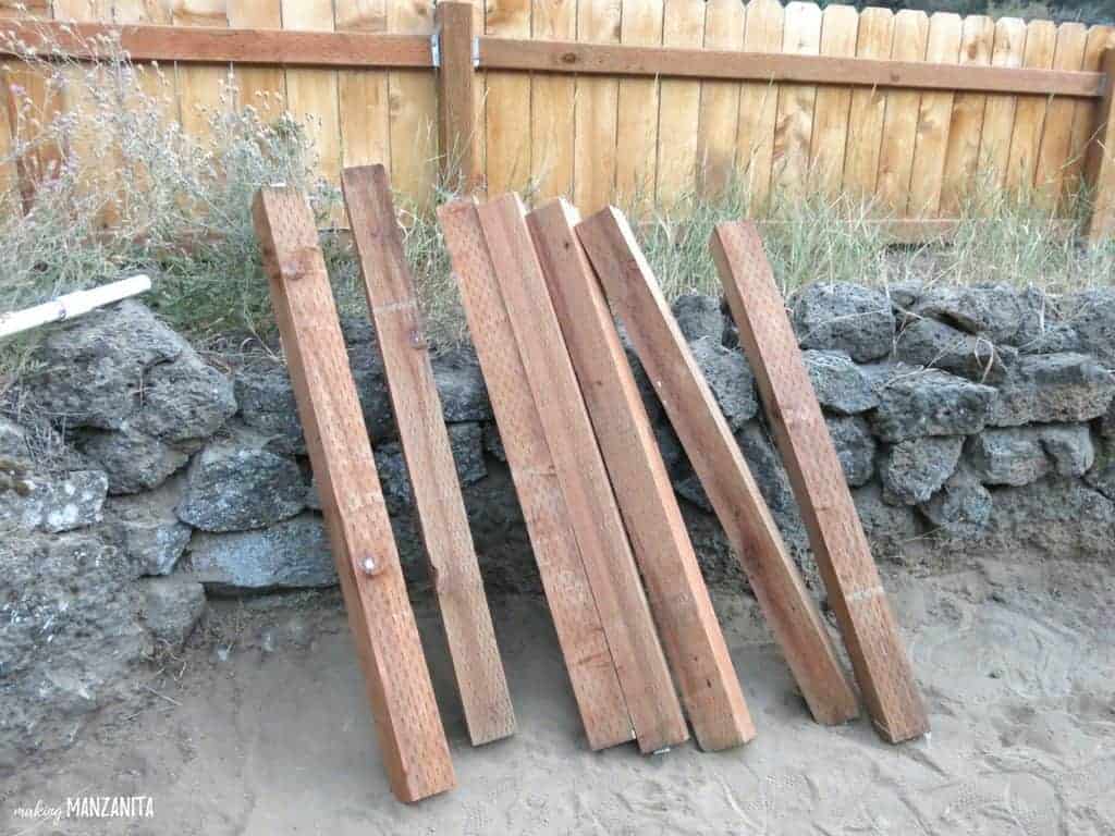 wood posts to be used as a corner supports for waist high raised garden beds leaning on the rock bed and wooden fence