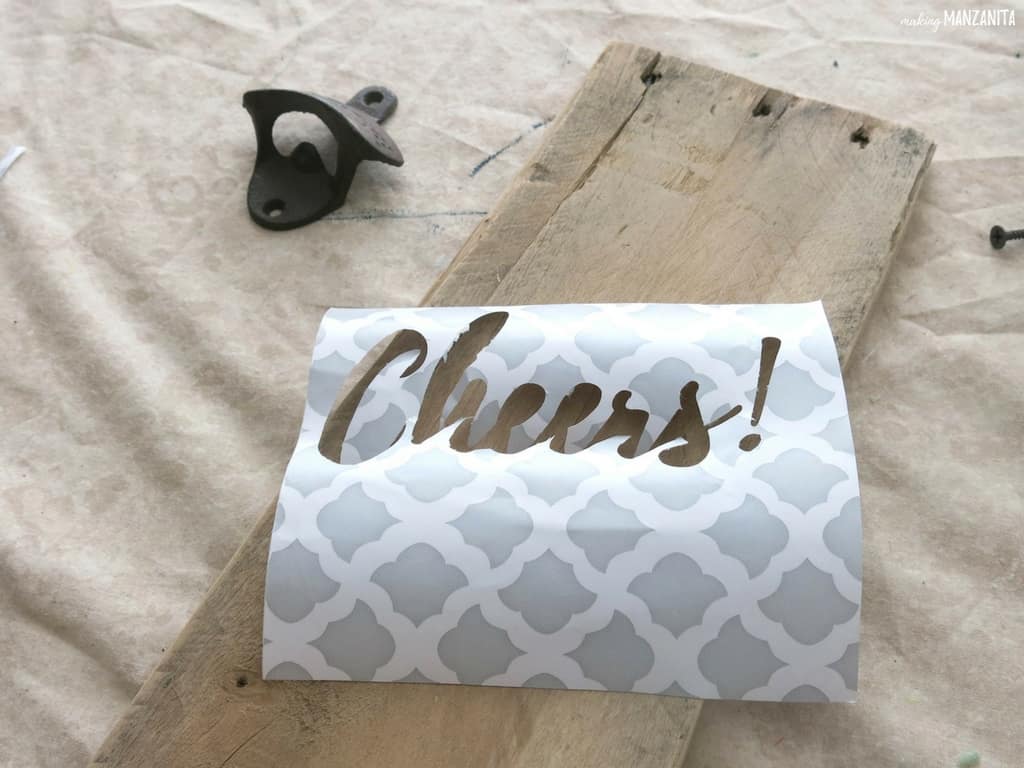 Schablone aus Kontaktpapier, das auf Palettenholz liegt und darauf wartet, bemalt zu werden, um einen DIY-Flaschenöffner herzustellen