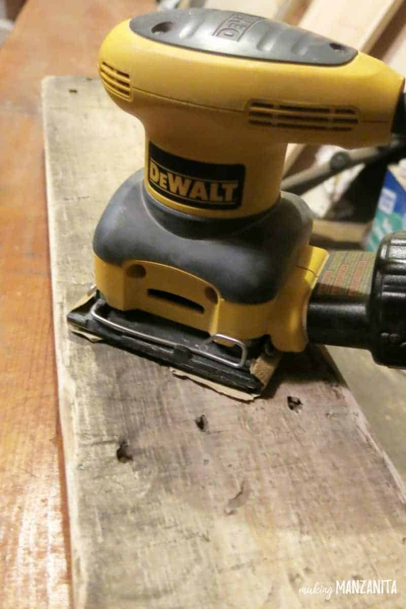 Using a DeWalt electric sander to sand down the wooden pallets